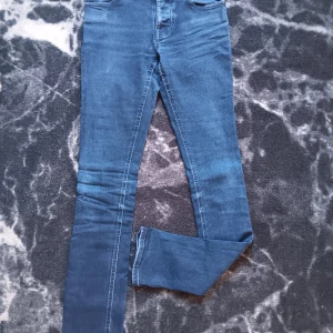 Mörkblå jeans från Nudie Jeans - Snygga mörkblå skinny jeans från Nudie Jeans med klassisk femficksdesign och tydliga sömmar på bakfickorna. Jeansen har hög midja och är tillverkade i stretchigt denim för en tight passform. Perfekta för dig som gillar stilrena och moderna jeans.