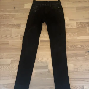 Svarta Replay Anbass jeans herr - Säljer ett par svarta Replay Anbass jeans med smal passform och klassisk femficksdesign. Byxorna har en modern skinny siluett och är tillverkade i stretchigt jeanstyg för extra komfort. Perfekta för dig som gillar stilrena och tajta jeans.