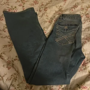 Blå jeans med stjärndetalj från Lindex - Snygga blå jeans från Lindex i storlek 158 med cool stjärnformad broderi på bakfickan och kontrastsömmar. Klassisk femficksmodell med knapp och dragkedja framtill. Jeansen har en rak passform och är tillverkade i mjukt denimtyg.Nyskick på dessa.