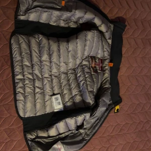 Svart dunväst från Parajumpers - Snygg svart dunväst från Parajumpers med quiltad design och gul detalj vid kragen. Västen har dragkedja framtill, två sidofickor med dragkedja och en bröstficka. Insidan är ljusgrå och materialet är polyester. Perfekt för lager-på-lager under höst och vinter, inga hål eller konstigheter , fler bilder kan skickas!🤗