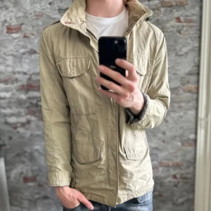 Field jacket - Säljer en beige parkajacka i srtl M. Märket ”Snoot”            med fyra stora fickor framtill och hög krage. Jackan har dragkedja och knappar, samt detaljer som D-ring och sydda sömmar. Perfekt för dig som gillar en clean och funktionell stil. ⚡️Skriv vid frågor eller fundering 999kr