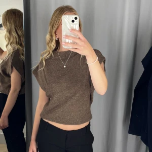 Brun stickad croppad topp - Säljer en brun stickad topp med croppad passform och ärmlös design. Toppen har en enkel, rak form och hög halsringning. Knappt använd!! 