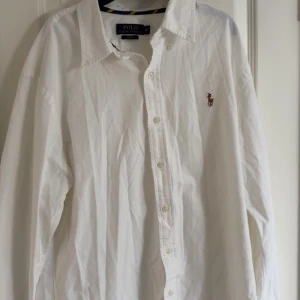 Vit skjorta Polo Ralph Lauren XL - Vit skjorta från Polo Ralph Lauren i slim fit-modell. Klassisk design med knappar framtill, lång ärm och broderad logga på bröstet. Tillverkad i bomull och passar perfekt för en clean och stilren look.