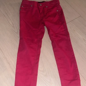 Röda byxor från Tommy Hilfiger - Snygga röda barnbyxor från Tommy Hilfiger med klassisk femficksdesign och silverfärgade nitar. Byxorna har rak passform och är tillverkade i mjuk bomull som är skön att ha på sig. Storlek för 4 åringar.