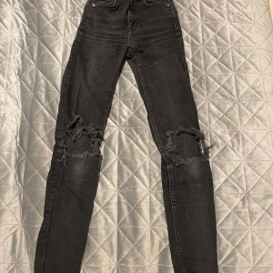 Svarta skinny jeans från Gina Tricot - Svarta 'Perfect Jeans' från Gina Tricot i skinny fit med slitna och trasiga detaljer vid knäna. Klassisk femficksmodell med knapp och dragkedja framtill. Jeansen är tillverkade i stretchigt denim för en tight och bekväm passform.
