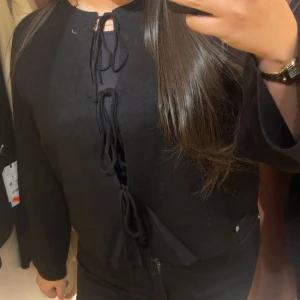 Svart kofta med snörning - Svart kofta med lång ärm och snygga snörningsdetaljer framtill. Koftan har en enkel, stilren design och är perfekt att slänga över en topp. Materialet känns mjukt och bekvämt mot huden.