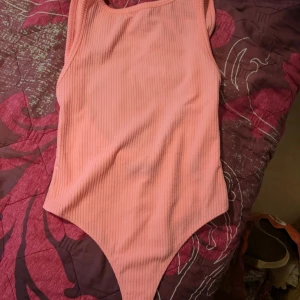 Ribbad rosa baddräkt/bodysuit  - Säljer en ribbad rosa baddräkt rån Bershka i storlek M. Toppen har ärmlös design och en snygg, enkel form som passar perfekt till jeans eller kjol. Materialet är mjukt och stretchigt för en bekväm passform.