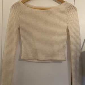 Beige stickad långärmad topp - Säljer en beige stickad topp med lång ärm och rund halsringning. Toppen har en croppad passform och ett snyggt strukturerat mönster i materialet. Perfekt att styla med jeans eller kjol för en trendig look.