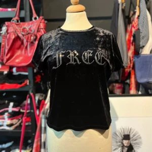 Svart sammets-topp med strass från H&M - Svart kortärmad topp i glansig sammet från H&M Divided, med texten 'FREE' framtill i strass. Rund halsringning och rak passform. Materialet är mjukt och huvudsakligen polyester med lite elastan för stretch.