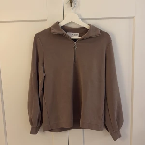 Brun half zip tröja från Selected Femme - Säljer en brun långärmad tröja från Selected Femme med halv dragkedja och krage. Tröjan har en loose passform och är tillverkad i mjukt material, perfekt för höst och vinter. Stilren och enkel att matcha med det mesta.