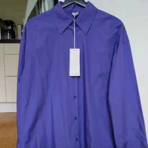 Skjorta från ARKET - Snygg lila skjorta från ARKET med klassisk krage och knäppning framtill. Skjortan är helt ny med prislapp. 