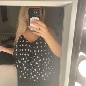 prickig topp - Säljer en svart ärmlös topp från Vila med vita prickar och flera lager volanger. Toppen har smala axelband och v-ringad hals. Luftig och flowy modell. Helt ny enbart provat 