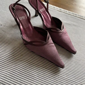  klackskor Lodi - Snygga vinröda klackar från Lodi med spetsig tå och låg klack. Skorna har en elegant omlott-design med smala remmar och spänne runt hälen. Endast använda på ett bröllop, jättesköna att gå i och perfekta för dans. Kartong och allt finns kvar