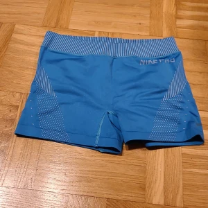 Blå Nike Pro Dri-Fit träningstights - Säljer ett par blå Nike Pro Dri-Fit shorts i storlek S. De har en tight passform, högmidjad design och är gjorda i ett stretchigt syntetmaterial. Snygga vita ränder och prickar på sidorna ger en sportig vibe. Perfekta för gymmet eller löpning.