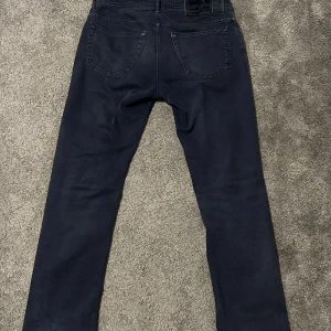 Jacob Cohen jeans 688 C - Snygga mörkblå jeans från Jacob Cohen med klassisk femficksdesign och diskret logga på bakfickan. Jeansen har raka ben och normal passform, tillverkade i mjukt bomullsmaterial med en exklusiv känsla. Perfekt för dig som gillar stilrena och tidlösa plagg. Storleken är W33. Hör av er vid minsta lilla frågor och priset är inte hugget i sten