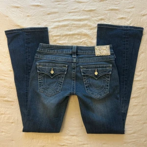 True Religion blå bootcut jeans - Ett par True Religion bootcut jeans med låg midja. Jeansen har fina pärl/sten detaljer (lite slitningar på pärlorna men syns ej på håll)  Innerbenslängd 78cm, midja rakt över 37cm. 