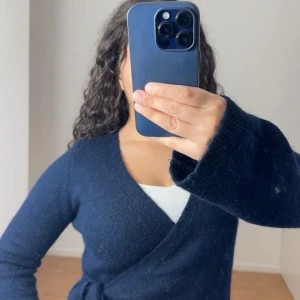 Mörkblå omlottkofta från Gina Tricot - Snygg mörkblå omlottkofta från Gina Tricot i mjuk ullblandning. Koftan har långa ärmar, v-ringad hals och knyt i sidan. Perfekt att slänga på över en topp när det är lite kyligt ute. 