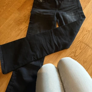 Svarta jeansbyxor från Gina Tricot - Svarta jeansbyxor från Gina Tricot med raka ben och snygga bakfickor med knappdetaljer. Klassisk femficksmodell och normal passform. Materialet är mjukt och stretchigt jeans, perfekt för dig som gillar stilrena och enkla byxor.