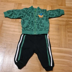 Bamse dress, byxa och tröja, by Lindex stl 62 - Svarta mjukisbyxor med gröna och vita ränder längs sidorna, samt Bamse-tryck på baksidan. Grön tröja med Bamse-tryck och dragkeja. 