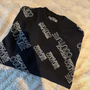 Svart sweatshirt  - Svart sweatshirt med vitt logotryck över hela tröjan. Rund hals, ribbade muddar vid ärmslut och nederkant. Tillverkad i mjuk bomull och polyesterblandning, perfekt för dig som gillar streetstyle och vill sticka ut. Som ny