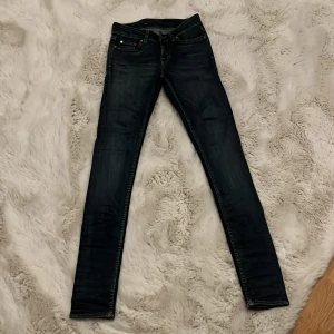 Mörkblå skinny jeans från Tiger Of Sweden - Snygga mörkblå skinny jeans från Tiger Of Sweden. Tillverkade i Italien. Jeansen har klassisk femficksdesign, kontrastsömmar och en brun läderpatch bak i midjan. Passformen är tight och midjan är normal. Perfekta för dig som gillar stilrena och smala jeans.