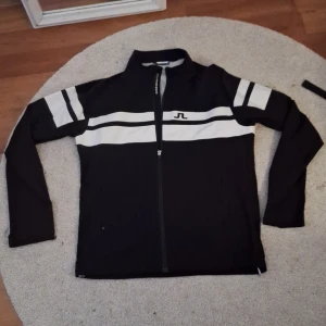 J.lindeberg vindjacka - Svart vindjacka från J.Lindeberg i storlek XL, men skulle säga att den passar L. Jackan har vita ränder över bröstet och armarna. Säljer då den inte passar, alltså helt oanvänd🙌🏼 Nypris ca 1800kr. Mitt pris 500kr‼️ Tveka inte att höra av er och skicka gärna prisförslag
