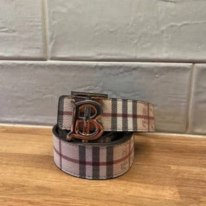 Rutig Burberry bälte med B-spänne - Snyggt bälte från Burberry med klassiskt rutig design i beige, svart och röd. Bältet har ett metallspänne med ett stort B i silverfärg. Perfekt accessoar för dig som vill ha en ikonisk och trendig look med lyxig känsla. Materialet är skinn med textilrutig yta. Äkta kommer med kvitto box och låda plånbok present men vet inte hur mycket