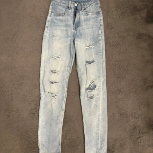 Ljusa ripped jeans från H&M, strl 34 - Säljer ett par ljusblå jeans från H&M i storlek 34 med snygga slitningar och hål på framsidan. Modellen är högmidjad, använd ett fåtal gånger! Skriv för fler bilder😊