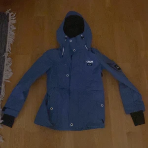 Blå skidjacka från Dope  - Säljer en blå skidjacka från Dope i storlek XS. Jackan har huva med snörning, vita detaljer på dragkedjor och knappar. Märket syns tydligt på bröstet och insidan. Perfekt för dig som gillar skidor och outdoor. Endast använd två veckor.