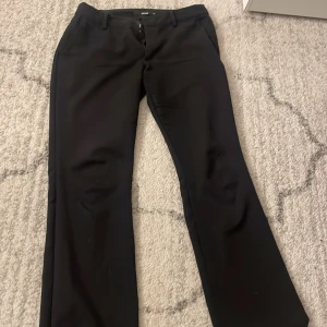 Svarta kostymbyxor bootcut - Snygga svarta kostymbyxor med bootcut-snitt och klassisk passform. Perfekta för en stilren look och passar till många olika outfits. Byxorna har hällor för bälte och stängs med dragkedja och knapp.