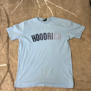 Ljusblå HOODRICH t-shirt - Snygg ljusblå t-shirt från HOODRICH med broderad logga i olika färger på bröstet. Klassisk passform med rund hals och korta ärmar. Perfekt för en chill och avslappnad stil.