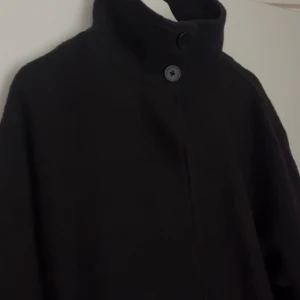 Svart kappa med hög krage och knappar - Svart ullkappa med hög krage. Från stockh LM i storlek xs men skulle säga att den passar S/M. 