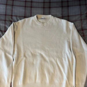 Vit stickad tröja från Zara - Säljer en stilren vit stickad tröja från Zara med rund halsringning och ribbade muddar. Perfekt för lager-på-lager och enkel att matcha med olika outfits. Klassisk modell med lång ärm och mjukt material.