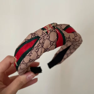 Diadem - Snyggt diadem i beige med klassiskt GG-mönster, gröna och röda ränder samt guldfärgade detaljer. Perfekt accessoar för att lyfta din look.