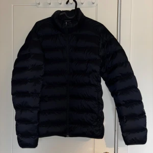 Svart dunjacka från Uniqlo  - Säljer en navy blå, ultralätt dunjacka från Uniqlo i storlek S. Jackan har en stilren, quiltad design med dragkedja framtill och långärmade ärmar. Perfekt för dig som vill ha en lätt och smidig jacka med snygg passform och enkel look.