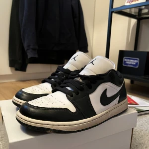 Nike Air Jordan 1 Low svart/vit - Nike Air Jordan 1 Low i svart och vitt skinn med klassisk Jumpman-logga på tungan och Air Jordan-broderi på hälen. De sitter skoskydd längst fram i tån