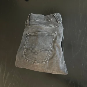 Replay Hyperflex Anbass svarta jeans - Svarta Replay Hyperflex Anbass jeans med snygg tvättad look och klassiska fem fickor. Stretchigt material för extra komfort och passform. Använt 1 gång. Har ett litet hål vid sidan som går lätt att sy ihop! Ordinarie pris ca 1200. Mitt pris- 399!