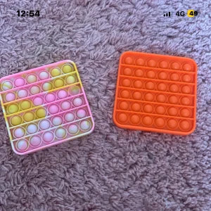 Pop it  - Bilden visar två pop it-leksaker i silikon, en i orange och en i pastellfärger. Perfekt för stressavlastning och sensorisk lek. Båda ser ut att vara i mycket gott skick utan synligt slitage eller defekter.
