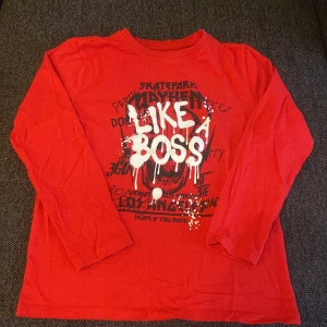 Röd långärmad tröja Like a Boss - Cool röd långärmad tröja med trycket 'LIKE A BOSS' i vitt och svart graffiti-stil på bröstet. Perfekt för dig som gillar streetwear och vill sticka ut. Skön passform och mjukt material, passar till chill dagar och häng med kompisar.