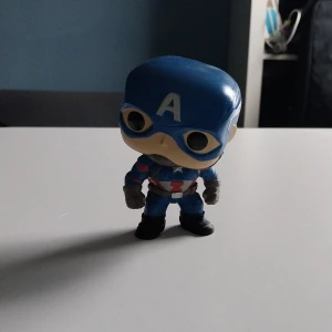 Funko Pop! Captain America - Snygg Funko Pop! figur av Captain America i klassisk dräkt med sköld. Figuren är i gott skick utan synliga repor eller skador. Perfekt för Marvel-samlaren eller som dekoration på skrivbordet. Levereras som på bilderna.