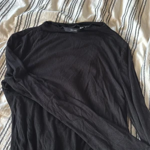 Svart ribbad långärmad topp Vero Moda - Det Svart långärmad topp från Vero Moda i storlek XS. Tröjan har ett ribbat tyg som ger en snygg struktur och sitter skönt mot kroppen. Enkel och stilren design med rund hals och smal passform, perfekt att matcha med jeans eller kjol.