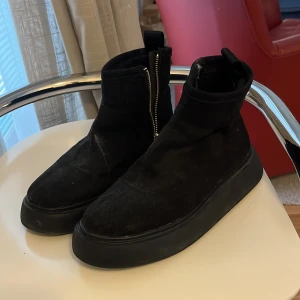 Svarta boots med dragkedja - Svarta boots från H&M med rund tå och platt sula. Skorna har en grov dragkedja på sidan och är tillverkade i mocka-liknande material. Stilren design med diskret flik baktill för enkel påtagning. Perfekt för dig som gillar minimalistisk look.