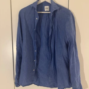 linneskjorta från Oscar of Sweden slim fit - Snygg blå skjorta från Oscar of Sweden i mjukt linne. Skjortan har klassisk krage, långa ärmar och knappar framtill. Perfekt för dig som gillar en chill och stilren look. Passar dig som vill ha en luftig och bekväm skjorta med enkel design.