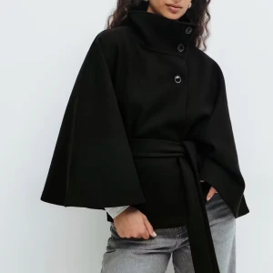 Svart kappa med bälte och hög krage - Svart kappa med cool hög krage och knappar framtill. Jackan har vida ärmar och ett matchande bälte i midjan för snygg siluett. Perfekt för dig som gillar minimalistisk stil och vill ha något som sticker ut. Materialet känns mjukt och har en lyxig känsla. Pris kan diskuteras har knappt haft på mig den 