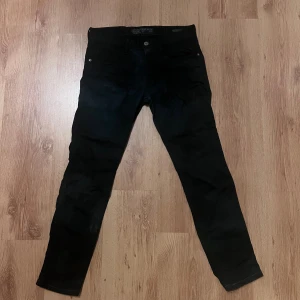 Replay Anbass svarta jeans, stl 31-32 - Svarta Replay Anbass jeans med klassisk femficksdesign och smal passform. Snygga detaljer som Replay-logga på bakfickan och läderpatch i midjan. Jeansen är tillverkade i stretchigt denim för extra komfort och har raka ben med normal midja. Jeansen är ok i skick har konstiga fläckar kan gå att tvätta bort.                Midja 41cm längd 95cm (71)