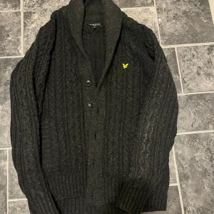 Svart vintage kofta från Lyle & Scott - Svart kabelstickad vintage kofta från Lyle & Scott. Storlek L men sitter som M.