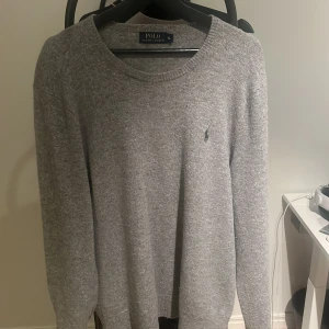 Grå stickad tröja Polo Ralph Lauren XL - Snygg grå stickad tröja från Polo Ralph Lauren i storlek XL. Klassisk rund hals och långärmad modell med den ikoniska broderade loggan på bröstet. Perfekt för dig som gillar stilrena och tidlösa plagg med soft vibe.
