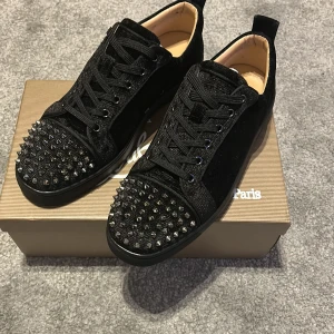 Svarta Christian Louboutin sneakers med nitar - Säljer ett par svarta sneakers från Christian Louboutin i sammet och skinn med ikoniska röda sulor. Skorna har snörning och är dekorerade med svarta nitar på tån för en edgy look. Kommer med originalkartong och tillbehör.  en sällsynt variant  använd 1 gång för inte var något som passade min still. kom gärna med bud och skriv vis funderingar kan gå med på ett billigare pris vid snabb affär 