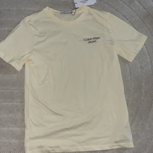 Ljusgul t-shirt från Calvin Klein Jeans - Snygg ljusgul t-shirt från Calvin Klein Jeans med diskret logga på bröstet. Klassisk rund hals och korta ärmar. 