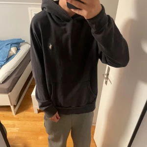 Blå hoodie från Polo Ralph Lauren - Blå hoodie från Polo Ralph Lauren med klassisk logga broderad på bröstet. Tröjan har huva, stor magficka och långa ärmar. Materialet är mjuk bomull som känns skönt mot huden. Perfekt för chill dagar och enkel att matcha med jeans eller sweatpants.